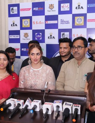 A group of people standing in front of a backdrop with various logos, giving a press conference. Several microphones from different news agencies are placed on a podium in front of them at Bizz Expo & Summit.